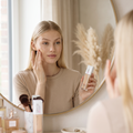 Frau trägt vor dem Spiegel Maybelline Superstay 24H Foundation auf, Foundation-Flasche und Pinsel auf dem Schminktisch