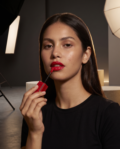 Maybelline Superstay Vinyl Ink Flüssiger Lippenstift, Model mit glänzend roten Lippen beim Auftragen