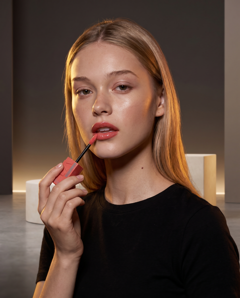 Maybelline Superstay Vinyl Ink Flüssiger Lippenstift, Model mit glänzend korallrosa Lippen im Studiolicht