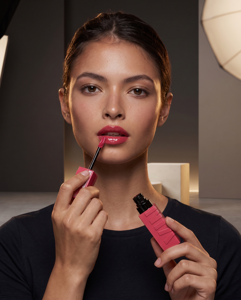 Model trägt Maybelline Superstay Vinyl Ink in glänzendem Pink und trägt den Lippenstift mit dem Applikator auf